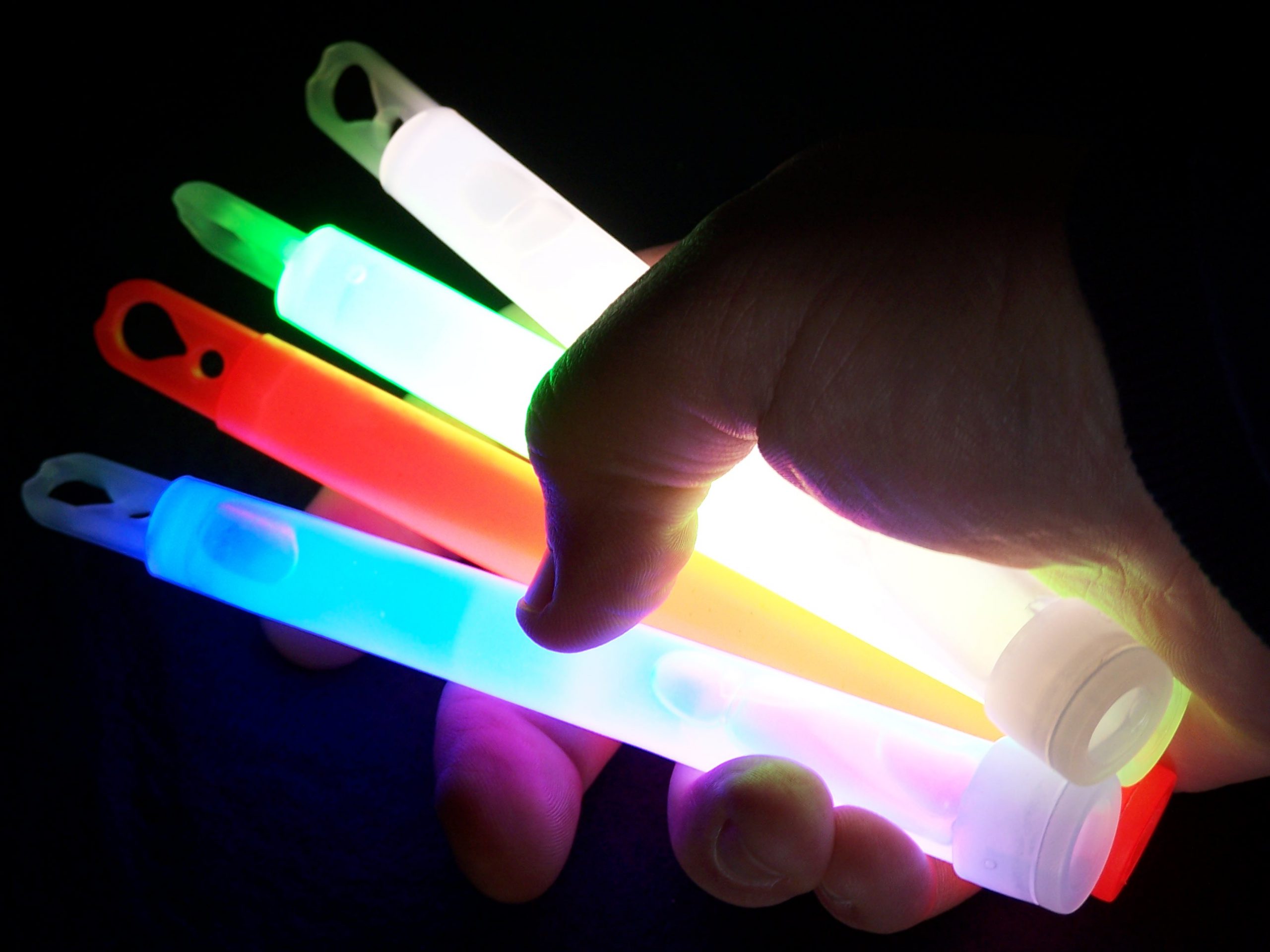A hand in the dark holding four different colored, glowing light sticks.