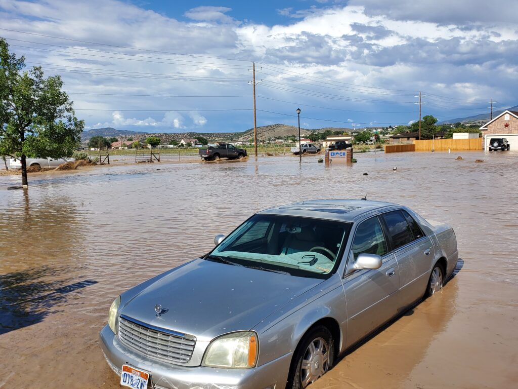 Car surrounded by muddy flood water up to it's door in an open parking lot.