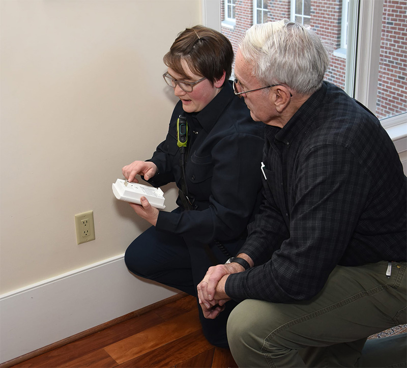 Woman helping elderly man install CO detector on wall.