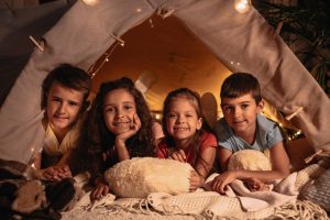 Group of children resting in handmade tent together at home