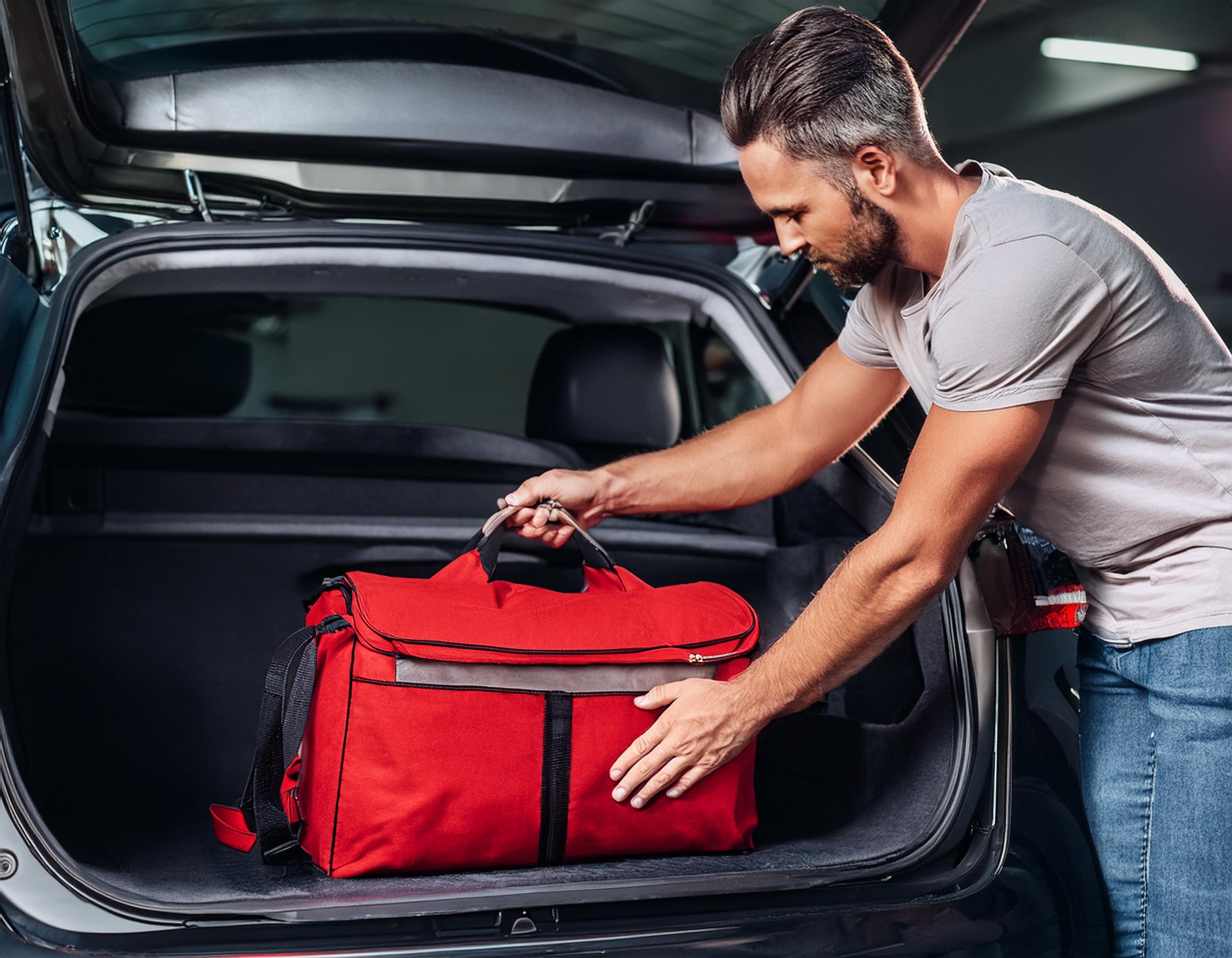 Man putting red duffle bag in open hatchback.