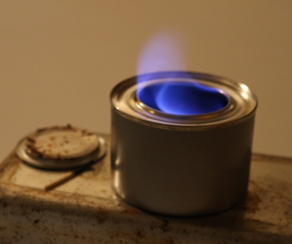 Open can of chafing gel fuel with lid beside can. Fuel is lit with a blue flame.