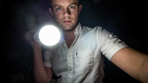 Image of a young man in the dark, holding a bright flashlight.