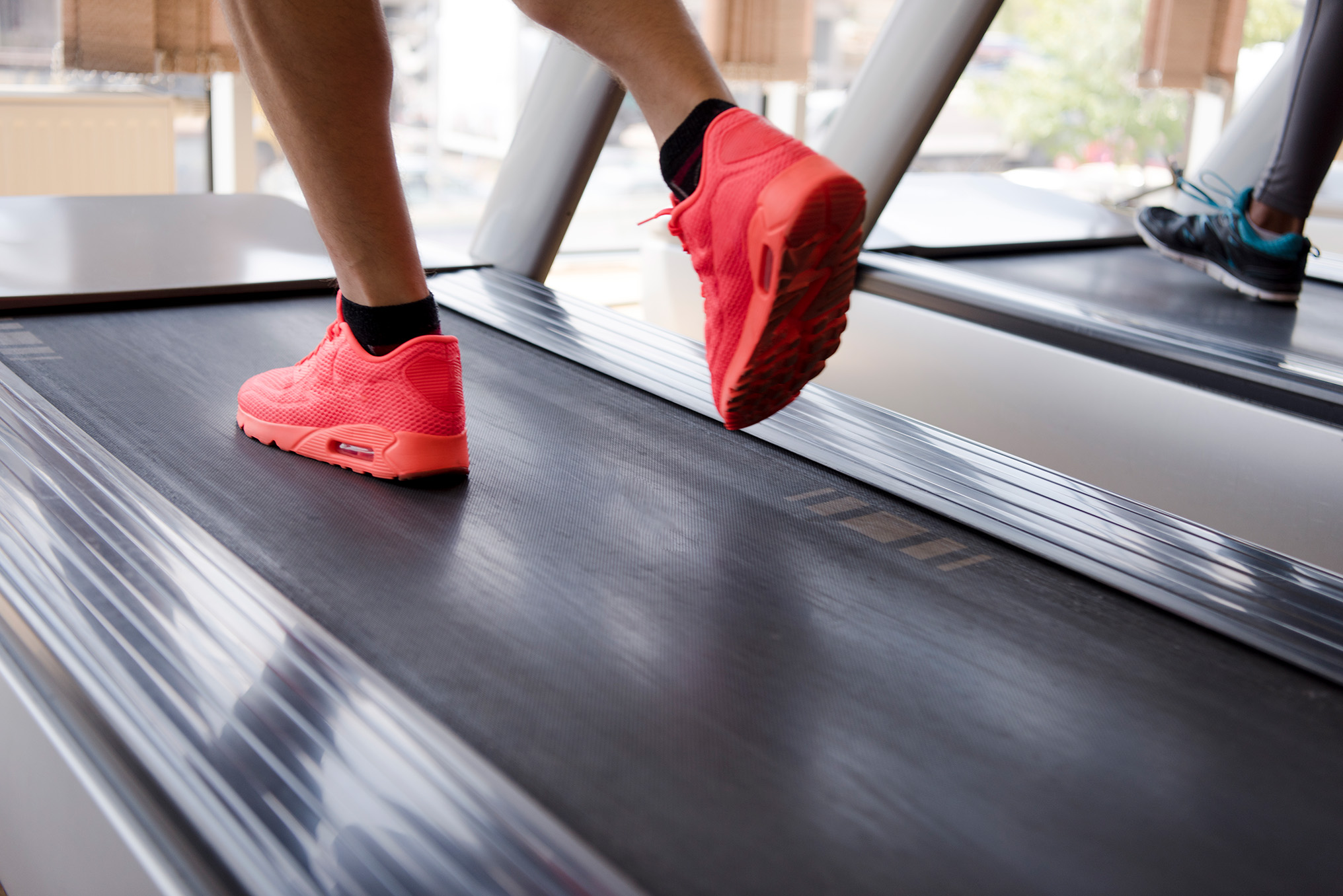 Man's legs in red shoes running on treadmill at gym.