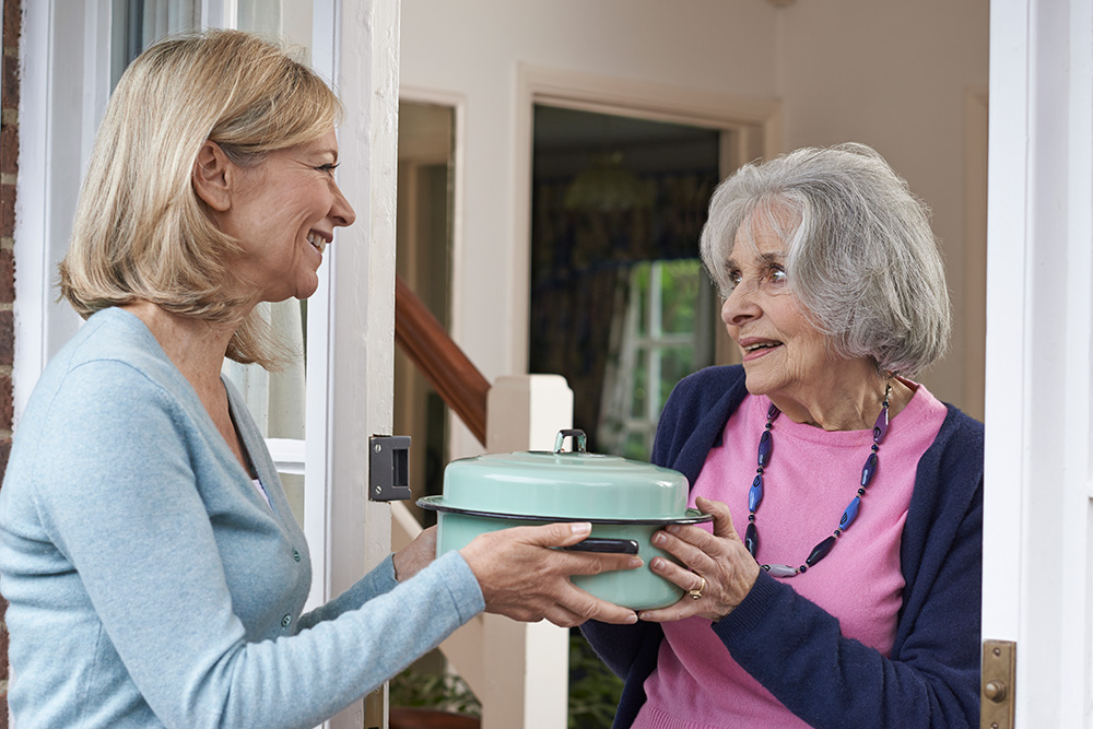 Woman sharing casserole dish with elderly neighbor.