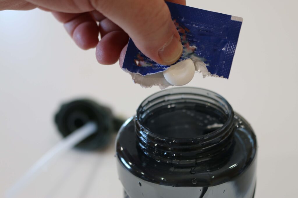 Hand holding a water purification tablet about to be dropped into a bottle full of water to be treated.