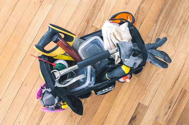 Image looking down into an open tool bag, lying on a hardwood floor, containing a variety of tools and safety equipment.